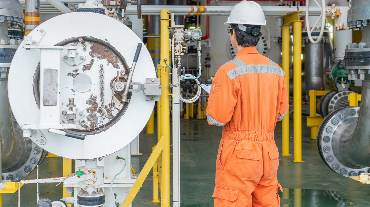 Oil & gas worker checking equipment, wearing orange coveralls and a white hardhat